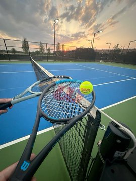 The image features two tennis rackets with tennis balls attached to them, placed near a fence or gate at a tennis court. The scene suggests that someone has recently finished playing tennis and left their equipment behind. This could be an indication of the popularity of tennis in this area, as it seems like many people enjoy the sport.