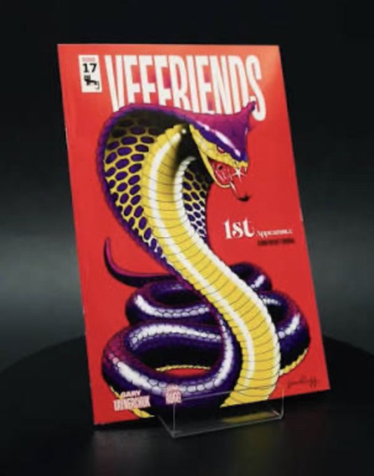 A red book cover with a purple and yellow snake, titled "Vfffrens", stands on a clear stand against a black background.