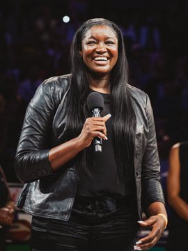 A woman with long dark hair smiles while holding a microphone on what appears to be a basketball court at Crypto.com Arena, likely celebrating a special player or person. This image perfectly complements the provided post, showcasing the individual being honored on a significant night.
