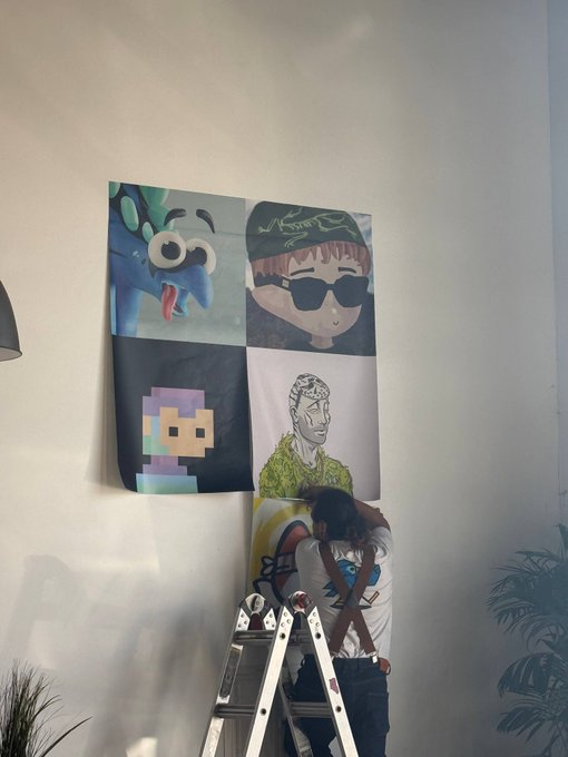 A person on a ladder works on a large multi-panel painting mounted on a white wall, featuring cartoonish characters including what appears to be a Minecraft Steve.