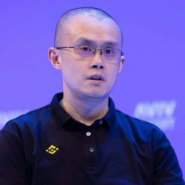 A man with short hair and glasses wears a black Lotto polo shirt, photographed against a purple background.
