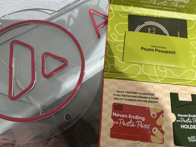 Olive Garden "Never Ending Pasta Pass" promotional materials laid out on a surface, including a "Pasta Passport," holder card, and informational packet, next to a metal Aviation Gin logo decoration.
