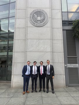Four young men in business suits pose for a group photo on the steps of a building that displays the seal of the United States Securities and Exchange Commission (SEC).