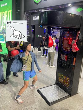 A child in a helmet and athletic wear prepares to punch a boxing machine at what appears to be a gaming or sports convention booth.