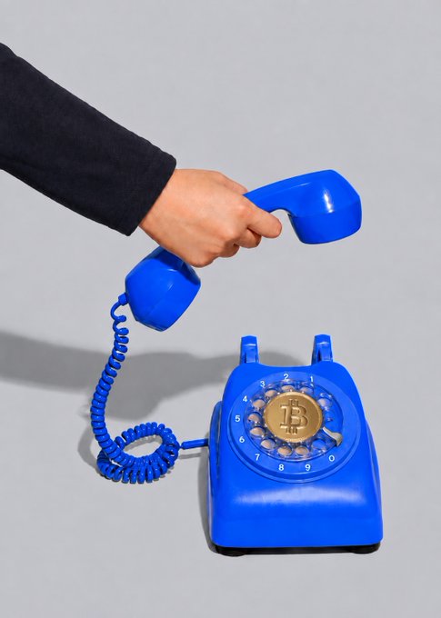 A hand lifts the receiver of a bright blue rotary phone, its dial filled with Bitcoin coins instead of numbers, symbolizing the incoming call of cryptocurrency's future. The golden "B" emblem at the center reinforces the message that Bitcoin is the next big thing "calling" investors to action.