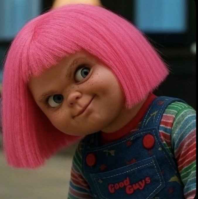 A doll with bright pink hair and a denim overall reading "Good Guys" offers a mischievous, wide-eyed smirk. The image humorously suggests a cheeky, rebellious undertone—possibly implying the poster's "now or never" stance on U.S. crypto leadership carries a sly, slightly unhinged energy.