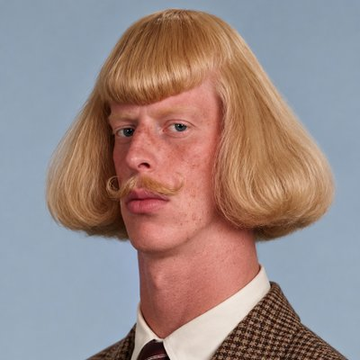 A man with a blonde bob haircut and curled mustache poses against a blue background, humorously embodying the "Jean Philippe" referenced in the post about the $JEANPHIL token dumping 68% from its all-time high of $10.61M.