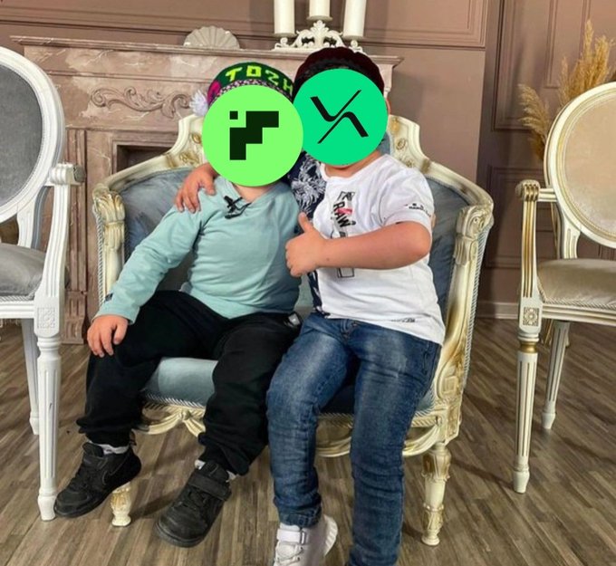 Two children sit on an ornate white and blue chair with their faces obscured by iRacing and Xbox logos, giving a thumbs-up in a formal setting.