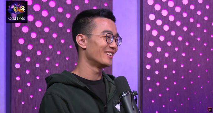Joe Weisenthal smiles beside a microphone during an Odd Lots interview with Jeff. An “Odd Lots” logo appears in the upper-left, and a small orange “B” mark is visible at the lower-right, accompanying the post’s comment about changing views on blockchain after speaking with Jeff.