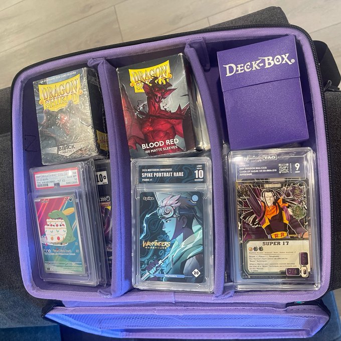 A purple 'DECK BOX' opened to show Dragon Shield card sleeves, graded Pokémon cards, and other trading card accessories.