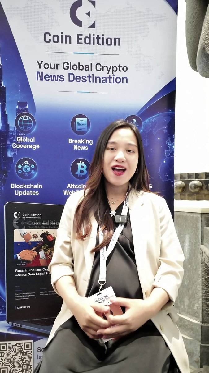 The image features a woman sitting down with her hands on her lap while wearing a black dress. She has a smile on her face as she poses for the camera. The background of the photo includes a banner that says "Coin Edition" and "Your Global Crypto News Destination". There is also an advertisement for a product, which appears to be related to cryptocurrency or digital currency.