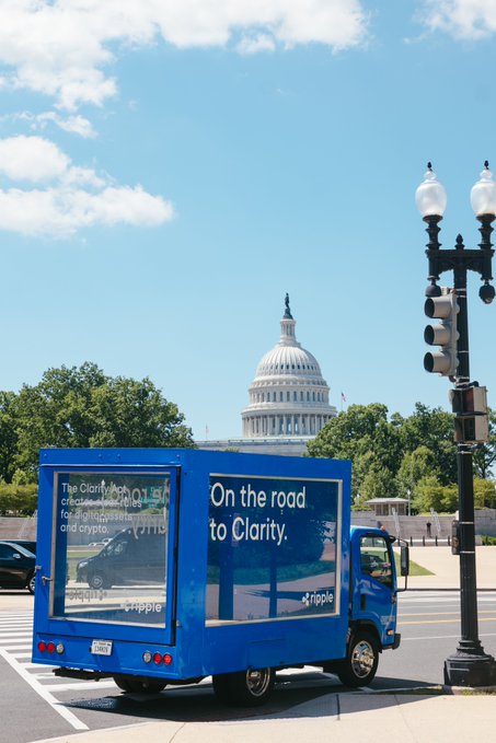 A blue Ripple-branded truck displays the message "On the road to Clarity" along with information about the Clarity Act protecting consumers and fostering responsible crypto innovation, parked in Washington D.C. with the U.S. Capitol building visible in the background as Congress works on digital asset legislation.