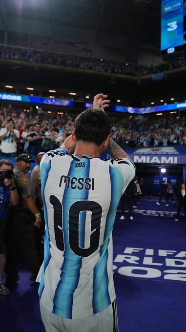 Lionel Messi wearing his Argentina #10 jersey (Inter Miami) applauding toward a cheering crowd inside a stadium, with 'MIAMI' and '3' visible on the signage.