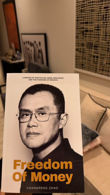 A copy of "Freedom Of Money" by Changpeng Zhao (CZ), featured alongside the tagline "A Memoir of Protecting Users, Resilience, and the Finding of Balance," is being held up in a home setting—fitting the post's theme of a new reader in Saudi Arabia sharing their excitement about the book and their growing crypto journey.