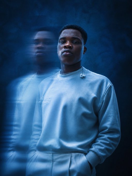 Moody portrait photograph of a young man in a light blue sweatshirt against a dark blue background with a reflection/echo effect of his image.