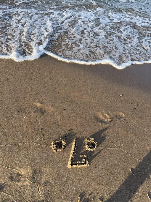 The word 'love' is written in the wet sand of a beach, with gentle ocean waves washing over it from the top of the frame.