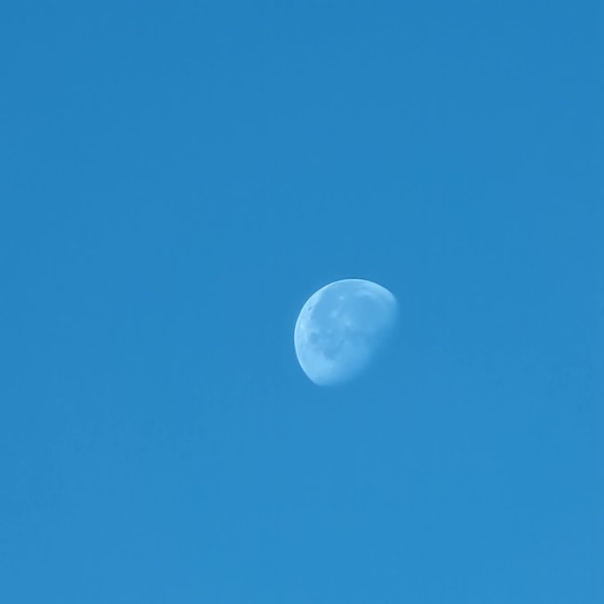 The image features a full moon in the sky, which appears as a large white circle against the backdrop of a clear blue sky. The moon's position and its bright illumination make it a prominent feature in the scene. The caption "Soon $Doge" is related to the image by placing it within a frame that includes the moon. This framing choice suggests that the image might be used for sharing on social media platforms or as part of an advertisement campaign, possibly promoting a product or service named " Soon Doge".