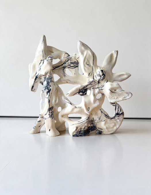 Abstract ceramic sculpture with organic, flowing shapes in white with black marbling, displayed on a white surface against a neutral background.