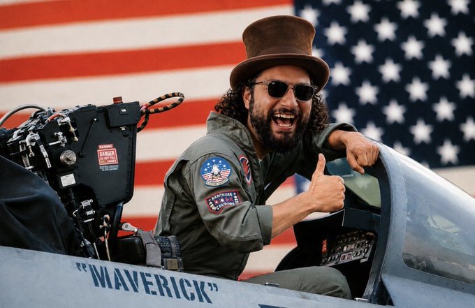 A man in a top hat and flight suit gives a thumbs up from the cockpit of a jet marked "MAVERICK," with the American flag in the background, possibly alluding to a "WONKA" space event.