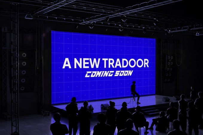 A stage event with silhouettes of an audience facing a large blue screen displaying 'A NEW TRADOOR COMING SOON'.