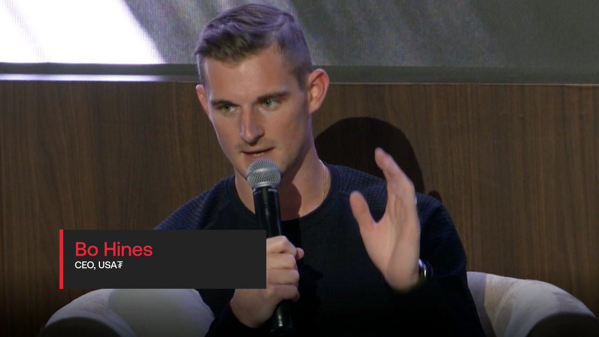 A man identified as 'Bo Hines, CEO, USA$' speaks into a microphone on a panel.