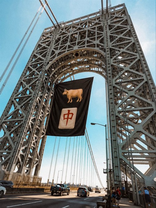 A photograph of the George Washington Bridge with a large black banner hanging from the tower, displaying a golden bull and the red Chinese character '中' (zhōng).