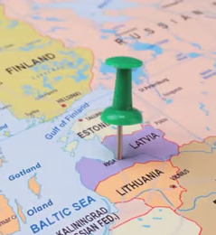 A green map pin is pinned on Latvia on a map of the Baltic region, highlighting the country whose central bank issued the new MiCA crypto licenses mentioned in the announcement.