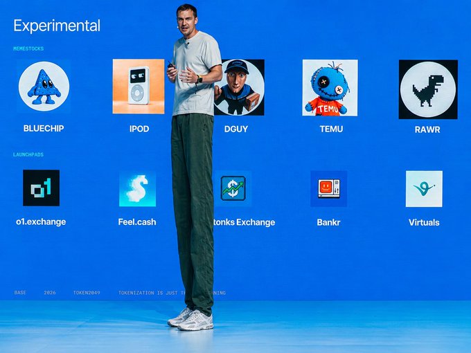 A man stands on a stage in front of a blue screen displaying 'Experimental' sections for 'Meme Stocks' (BLUECHIP, IPOD, DGUY, TEMU, RAWR) and 'Launchpads' (o1.exchange, Feel.cash, tonksExchange, Bankr, Virtuals).