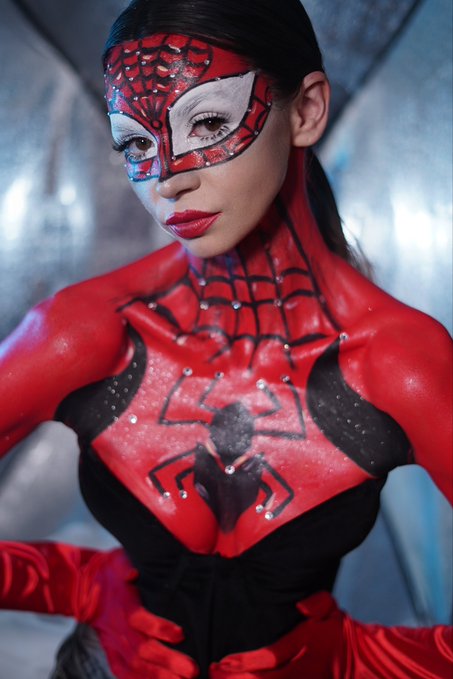 A cosplayer poses in a detailed red and black Spider-Man costume with a rhinestone-covered mask and chest emblem.