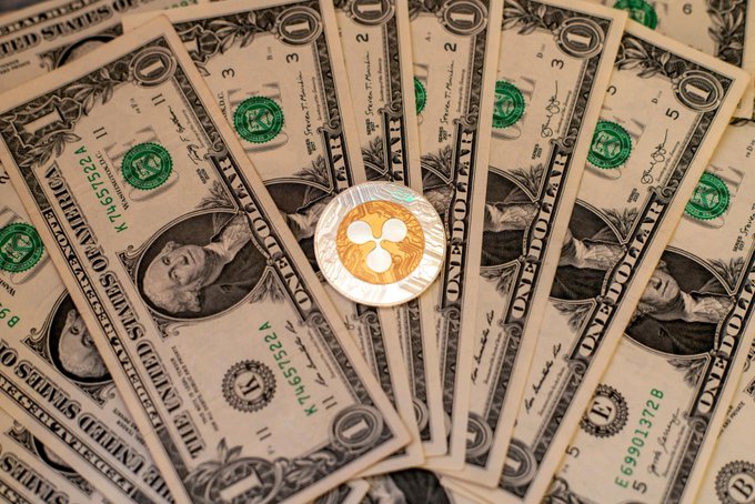 "This is a photo of a pile of money featuring $10 and $1 bills, with one of these $1 bills bearing a silver coin with three holes sitting right next to them. The caption of the image suggests that Ripple has been involved in a massive $1,000,000,000 XRP Treasury raise."