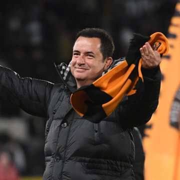A smiling man in a black puffer jacket holds up a black and orange scarf, appearing to celebrate at a sports venue, with the post's comment about reducing holdings by half possibly referencing the team's orange and black color scheme or its large fan merchandise presence.