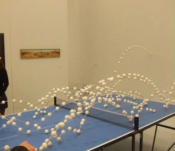 An art installation featuring an arched structure made of white spheres connected by strings, displayed on a blue platform in a gallery.