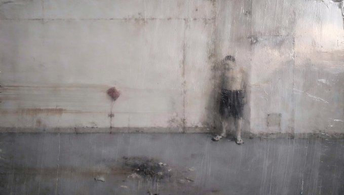 A blurry, rain-streaked image showing a person standing against a light-colored wall.