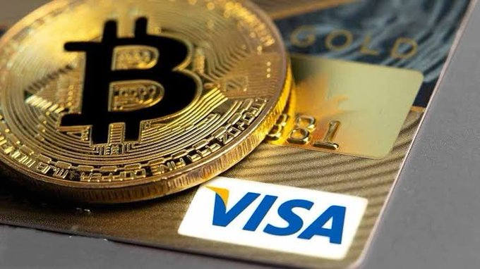A close-up of a physical gold Bitcoin coin resting on a gold Visa credit card.