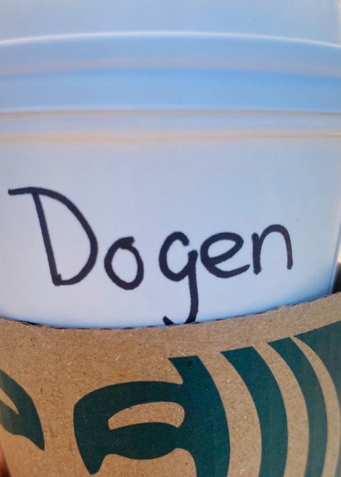 A Starbucks cup sleeve is shown wrapped around a white cup with the name "Dogen" written in marker, fitting the "gm legends" caption by featuring a classic Starbucks cup labeled with a name.