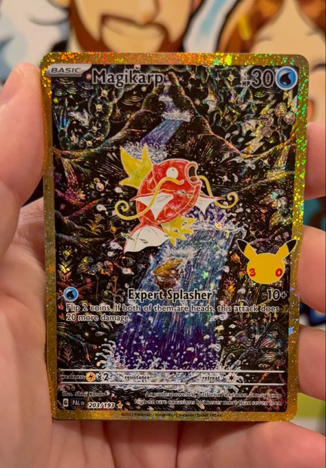A hand holding a shiny gold-bordered Pokémon trading card featuring Magikarp with the 'Expert Splasher' attack, which states 'Flip 2 coins. If both of them are heads, this attack does 20 more damage.' The card shows 230/195 with a gold star marking it as a rare.