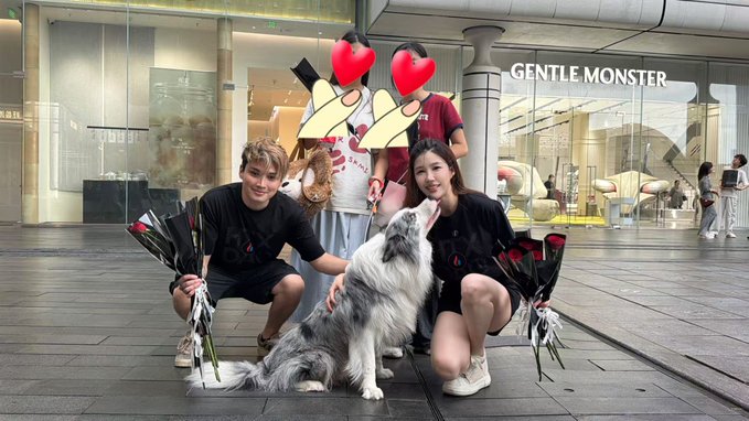 Two people posing with a fluffy gray and white dog in front of a 'GENTLE MONSTER' store, with two other people standing behind them whose faces are obscured by red heart emojis.