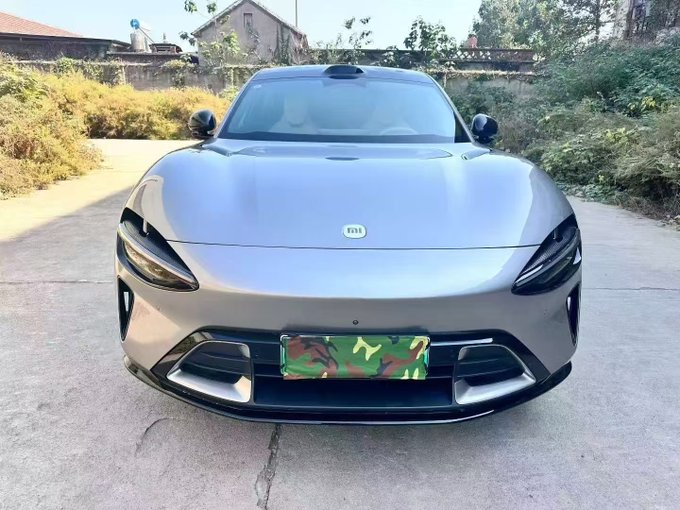 A silver/grey car parked outdoors with a green camouflage-patterned license plate.