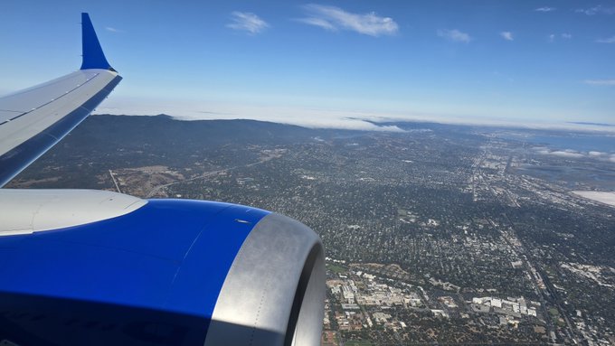 An aerial view from an airplane window showing the engine and wing above a sprawling city landscape near the coast.