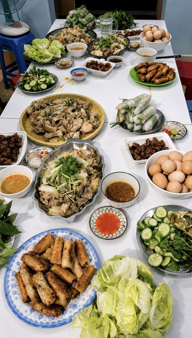 A Vietnamese family feast is spread across the table featuring spring rolls, fried rolls, chicken with herbs, pickled vegetables, cucumbers, and various dipping sauces. The post's playful invitation to head to "Tin Gấu" (Bear Radio) sets a casual, social tone that matches the abundant, communal spread ready for a gathering with friends.