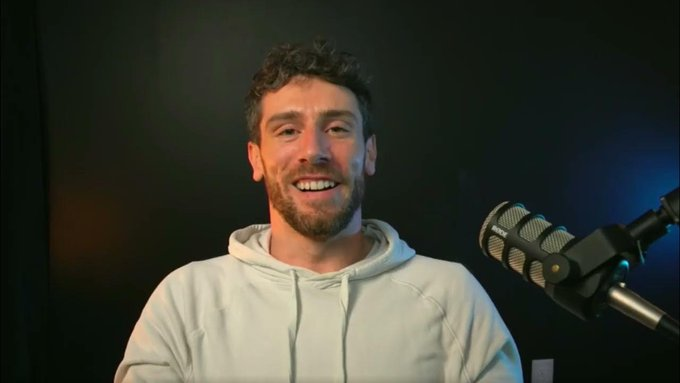 A bearded man in a light hoodie smiles in front of a professional podcast microphone against a dark backdrop, appearing to deliver commentary on TRON DAO's enterprise treasury settlement solutions.