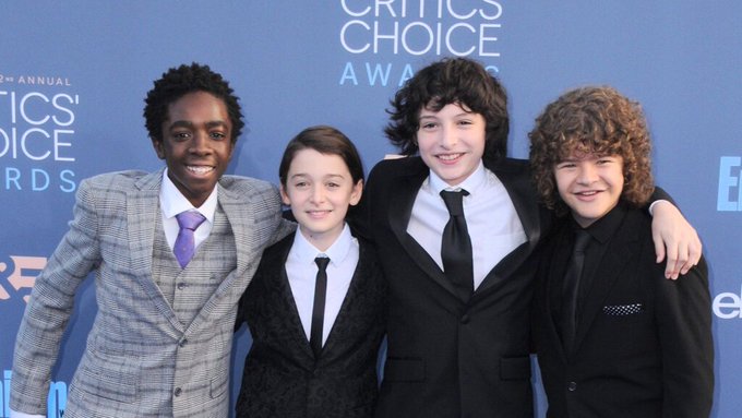 Four boys in suits pose together at the Critics Choice Awards with the backdrop reading 'CRITICS CHOICE AWARDS'.
