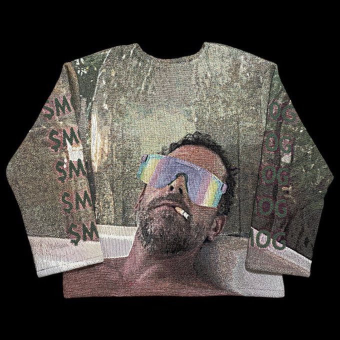 The image features a sweater with a man's face printed onto it, wearing sunglasses and a beard. The sweater has a green background that includes text such as "S M", "OG", and "OG". This unique design of the sweater is likely intended to be humorous or playful, possibly referencing a popular meme or trend in recent years.