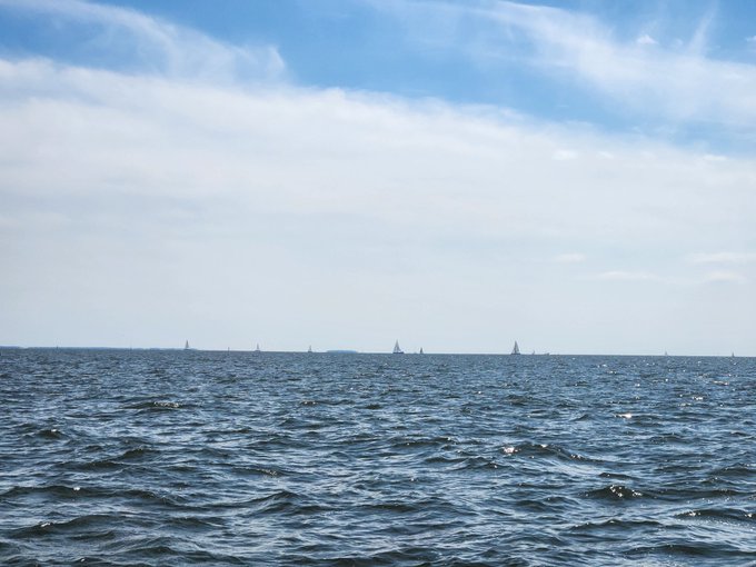 Sailboats glide along a distant horizon line over a vast, wave-tossed sea under a wide sky streaked with wispy clouds. The image perfectly mirrors the post's nautical references to "GM CT" and "GMI," which are sailing-related terms often used in cruising communities to greet fellow boaters during the September sailing season.