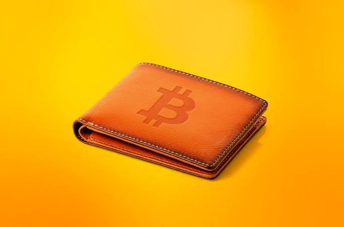 A brown leather wallet embossed with the Bitcoin '₿' symbol against a bright yellow background.
