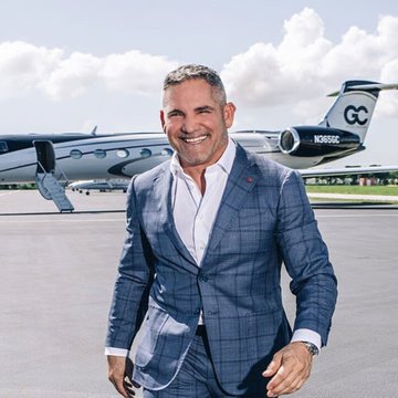 A man in a blue plaid suit stands smiling on an airport tarmac with a private jet bearing the tail registration 'N3059C' visible behind him.