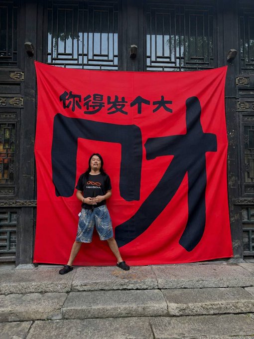 A person poses in front of a large red banner displaying the Chinese characters "你得发个大财" (meaning "You must get rich/lucky"), set against a traditional wooden architectural background, celebrating NeoSoul's announcement of completing an $11 million Pre-A funding round backed by top-tier institutions including MH Ventures, Amber Group, ArkStream Capital, 0G Foundation, and Kirin Capital.