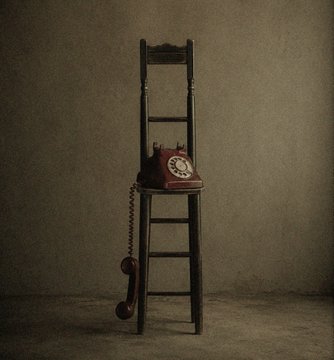 A moody still-life photograph of a vintage red rotary telephone mounted on a tall wooden ladder against a textured, dimly lit background.