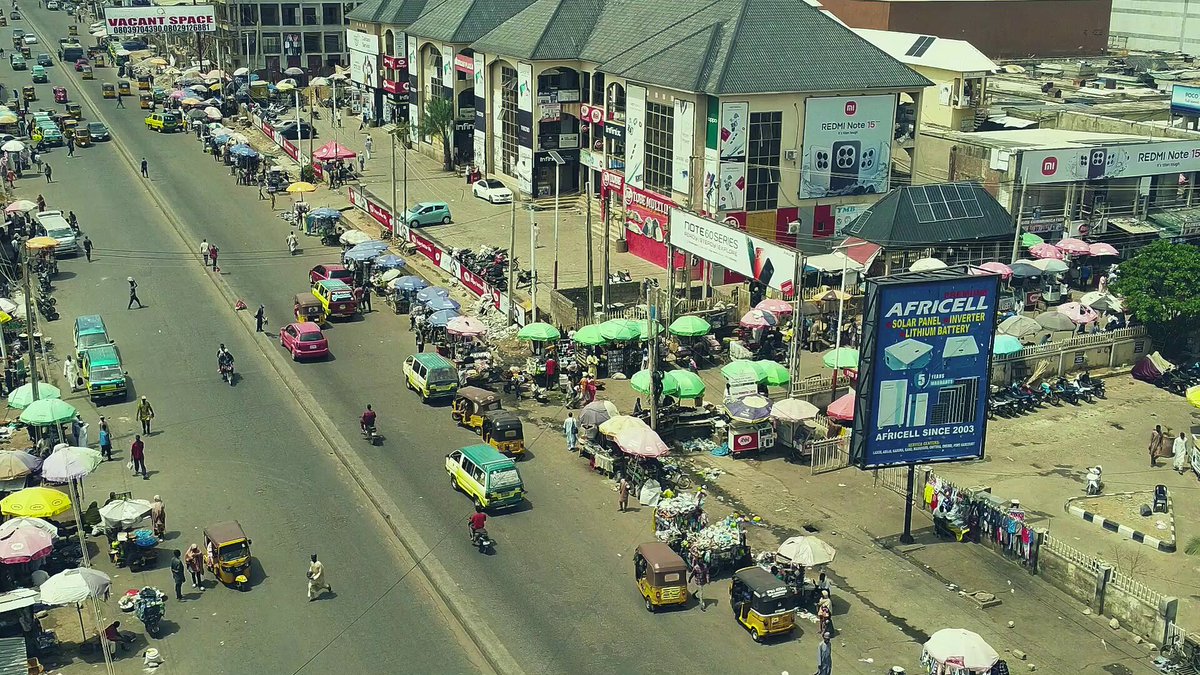iced tea stands line a busy street, with people walking and sitting under colorful umbrellas amidst shops and buildings.