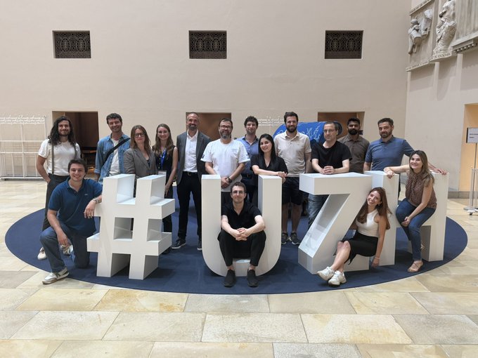 Group photo of a team posing behind large white '#EU24' letters in a grand hall, commemorating a 2024 European event.